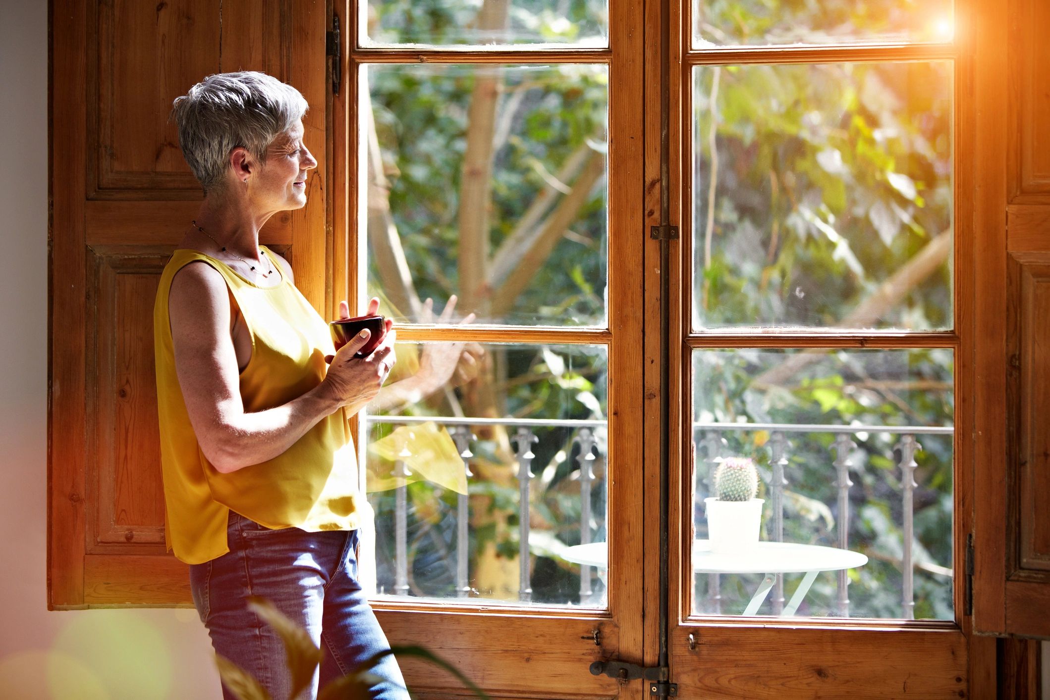 Mature woman standing by a window at home holding a warm drink